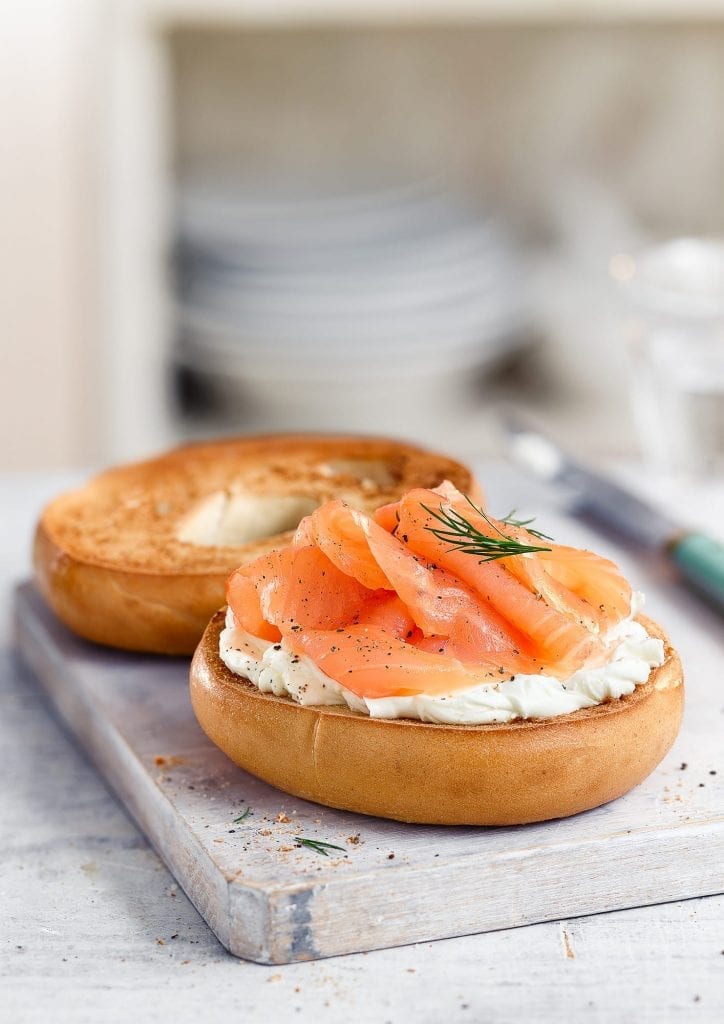 Salmon bagel with creme fraiche on chopping board